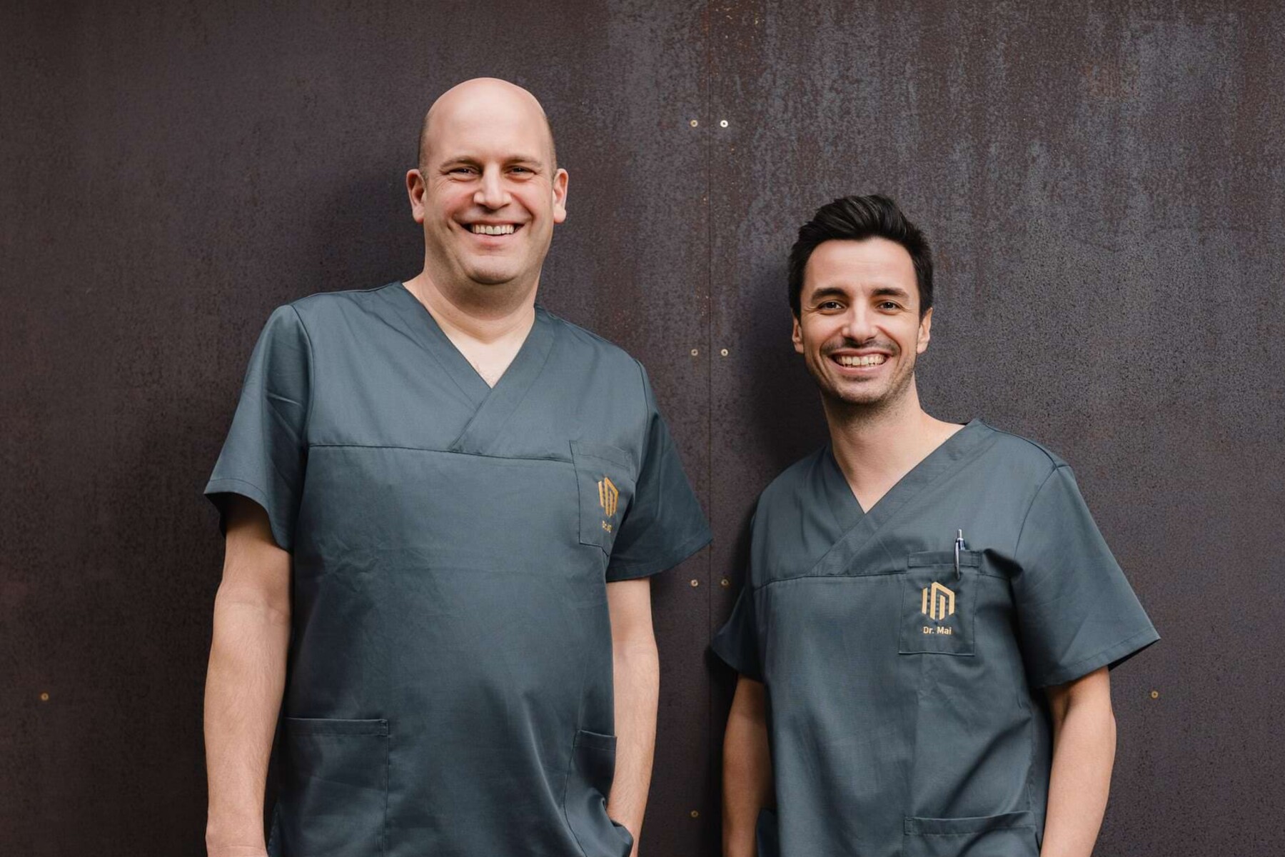 Die Inhaber der Praxis &ndash;&nbsp;Dr. Florian Will und Dr. Alexander Mai &ndash; stehen vor dem Praxisgeb&auml;ude ins Kasaks und lachen freundlich in die Kamera.