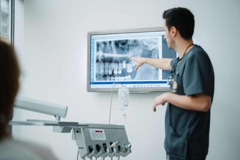 Zahnarzt zeigt auf Zahnimplantat auf R&ouml;ntgenbild in der Praxis in W&uuml;rzburg.