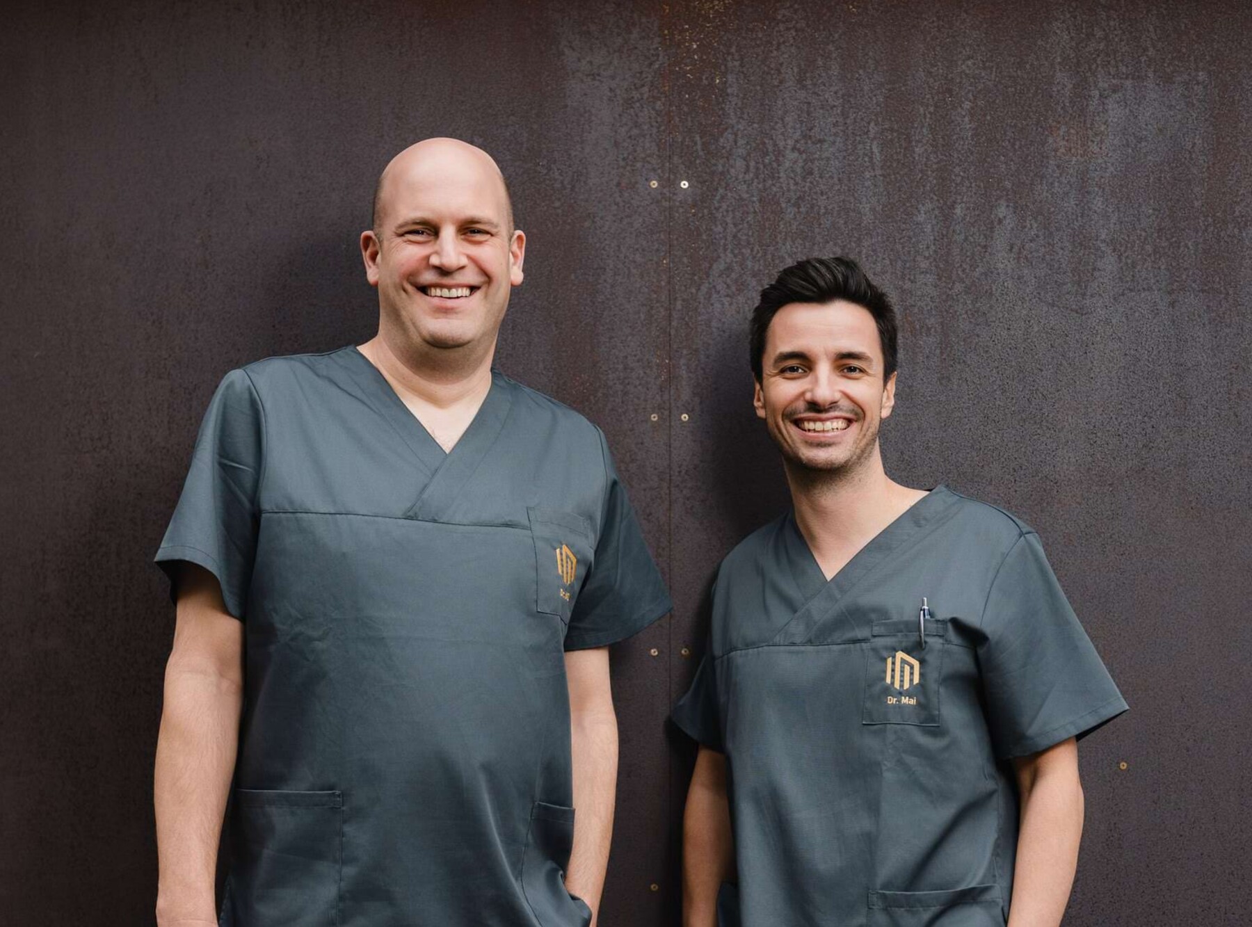 Freundliches Portrait von Dr. Will und Dr. Mai in schwarz/grauen Kasacks au&szlig;en vor dem Praxisgeb&auml;ude