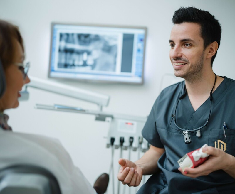 Dr. Alexander Mai mit einem Zahnmodell in der Hand, w&auml;hrend er einen Eingriff erkl&auml;rt.