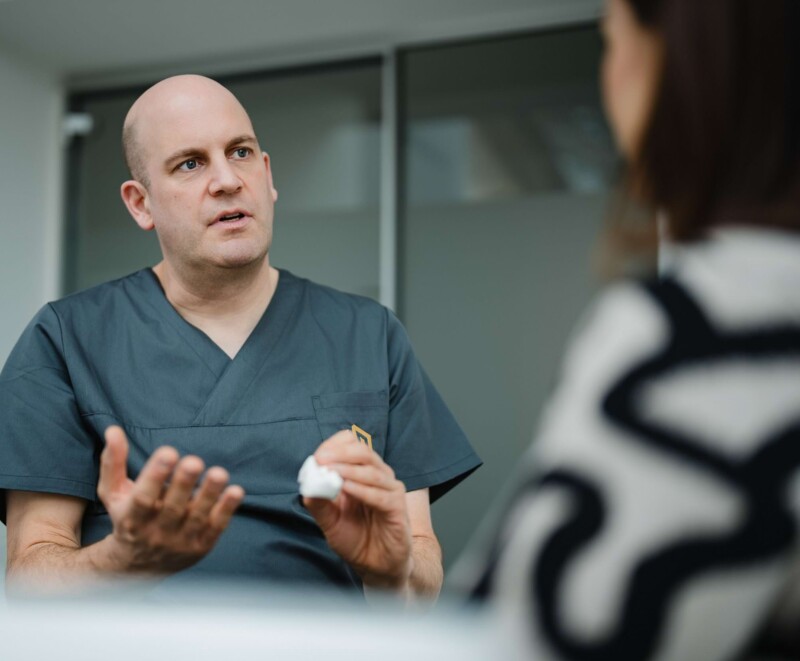 Dr. Florian Will mit einem Zahnmodell in der Hand, w&auml;hrend er einen Eingriff erkl&auml;rt.